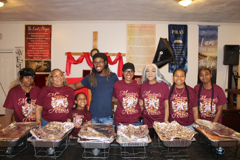 The Maxine’s Arms team in matching maroon shirts standing behind a long table of catering trays, ready to serve.